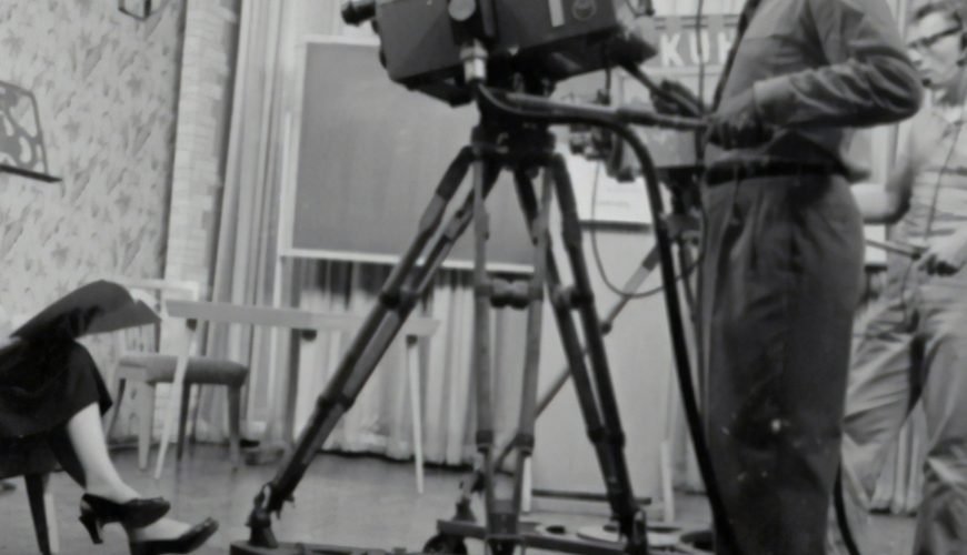 grayscale photography of man standing near studio camera and woman sitting while holding book