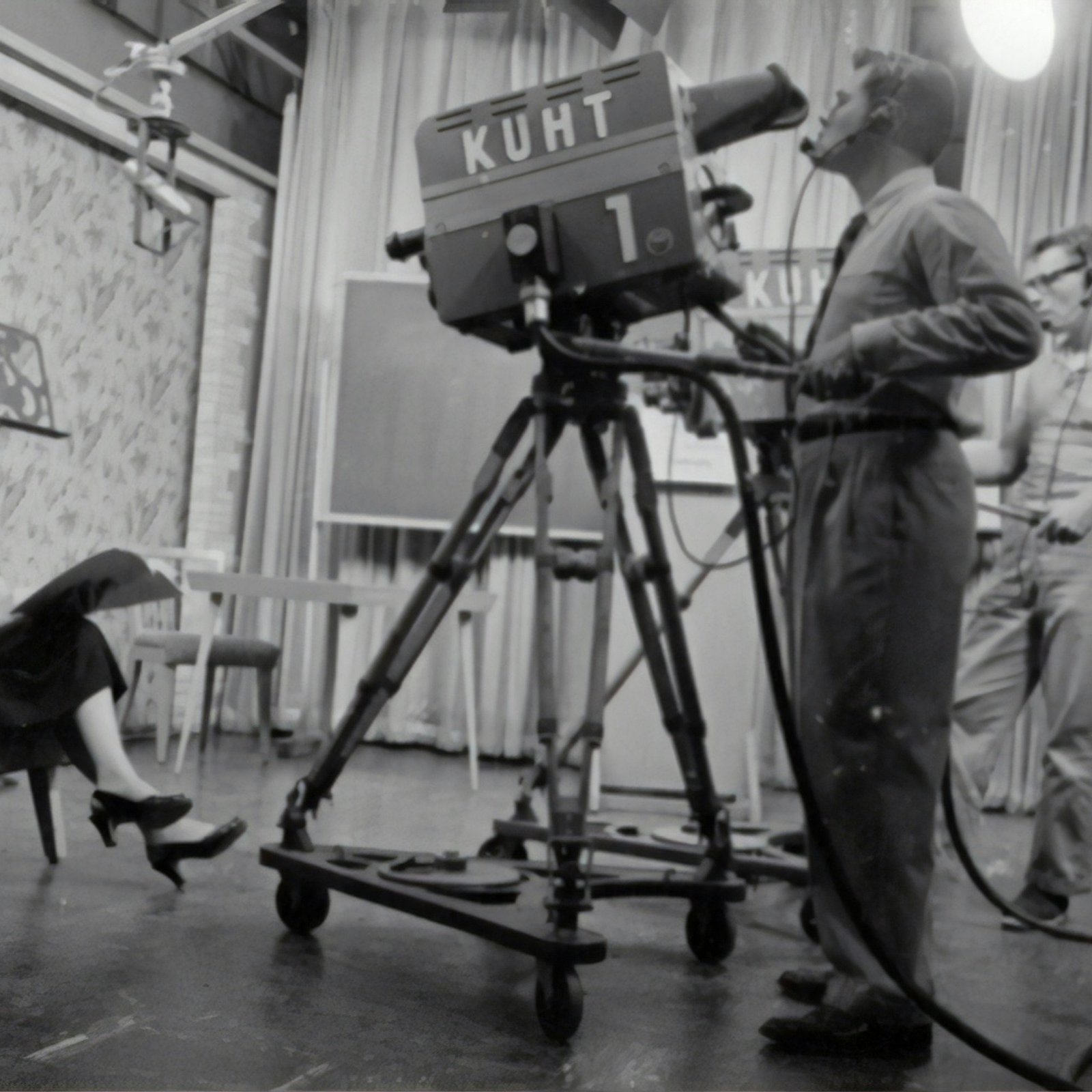 grayscale photography of man standing near studio camera and woman sitting while holding book